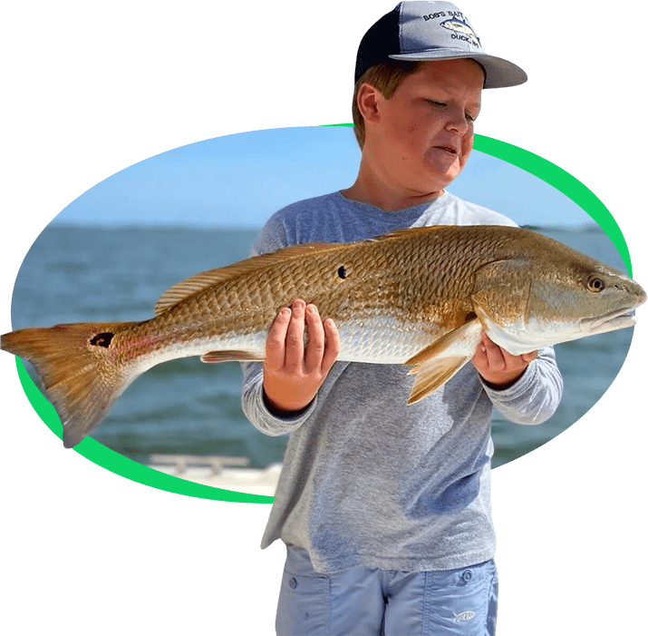 A young boy holding a large fish with both hands, proudly displaying his catch by the shoreline.